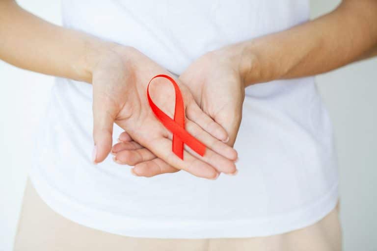 Woman hand holding red ribbon HIV, world AIDS day awareness ribbon.